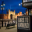 A photo of Southampton's city center at night. In the foreground, there's a sign that says "Bars to Unwind". The background reveals the city's landmarks, including the medieval city walls and the iconic Bargate. There are also streetlights and benches.